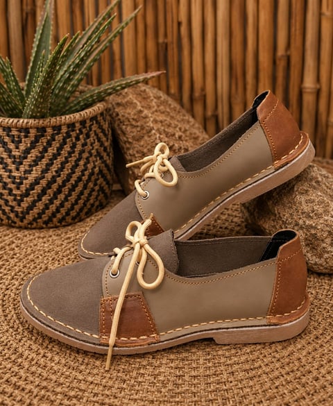 Pair of two-tone brown and tan leather lace-up loafers on a woven mat with a potted succulent plant in the background